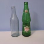 A clear glass early J. McLaughlin soda water bottle and green Canada Dry bottle